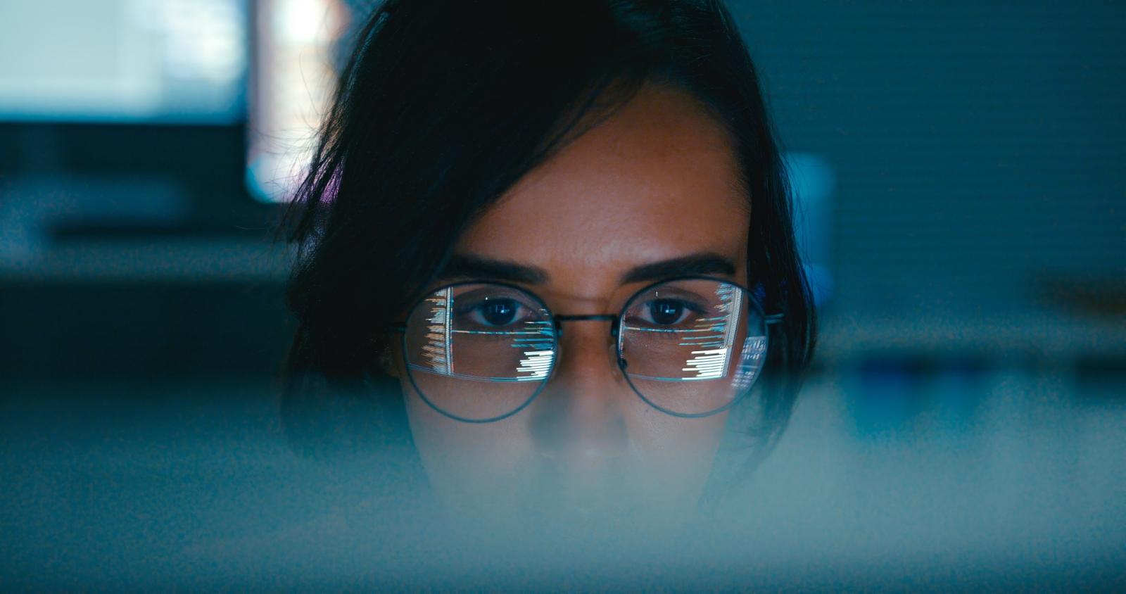 Web developer wearing glasses with code reflection on lenses, focused on computer screen