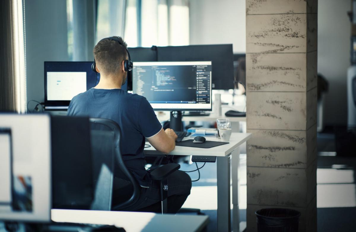 Web developer working at desk with multiple monitors displaying code and design applications