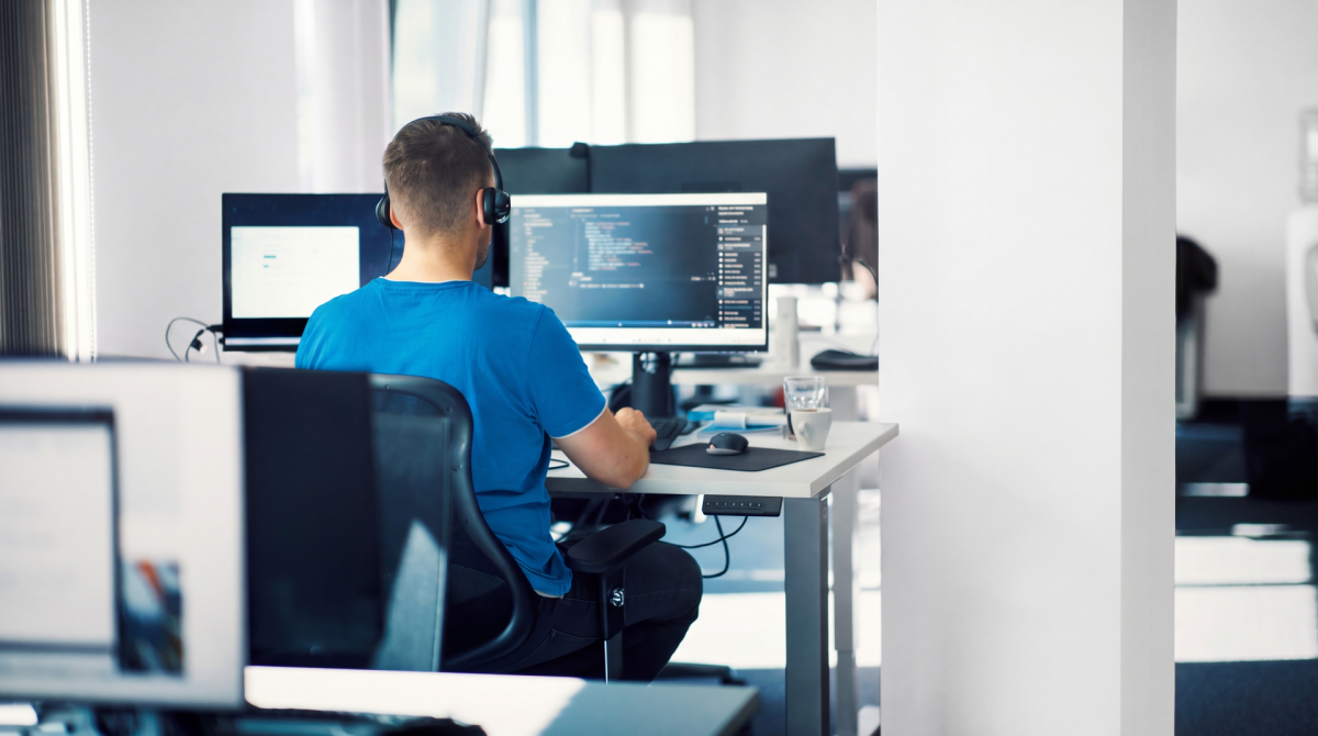 Web developer working at desk with dual monitors displaying code and applications